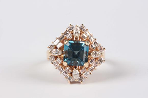 TooveysA gold, blue topaz and diamond cluster ring, claw set with the cut cornered square cut blue topaz within a surround of marquise, baguette and circular