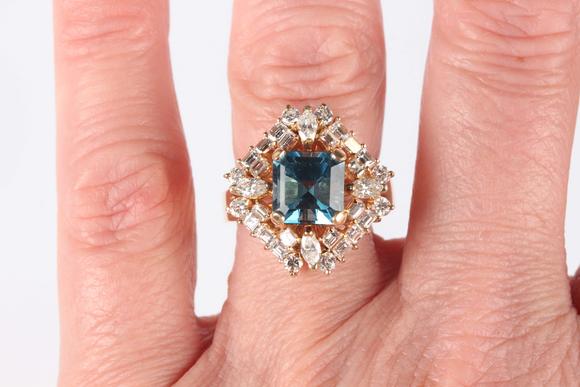 TooveysA gold, blue topaz and diamond cluster ring, claw set with the cut cornered square cut blue topaz within a surround of marquise, baguette and circular