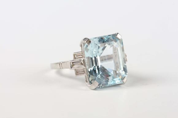 TooveysA platinum, aquamarine and diamond ring, claw set with the large cut cornered rectangular step cut aquamarine between baguette cut diamond three stone
