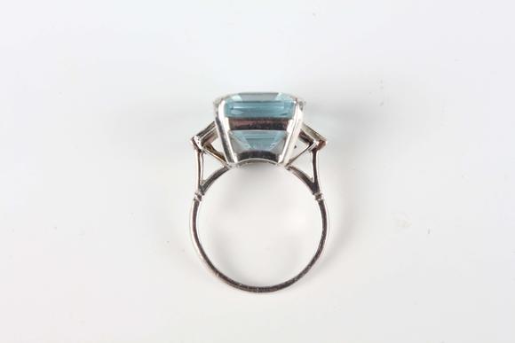 TooveysA platinum, aquamarine and diamond ring, claw set with the large cut cornered rectangular step cut aquamarine between baguette cut diamond three stone