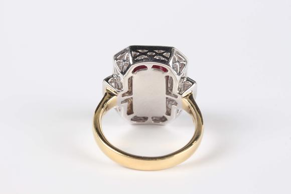 TooveysAn 18ct two colour gold, ruby and diamond cluster ring, collet set with the cut cornered rectangular step cut ruby within a surround of baguette and c