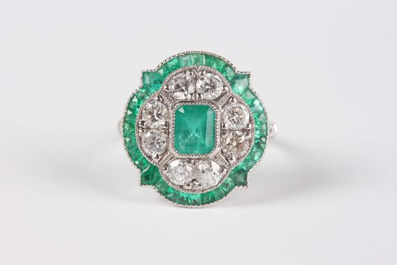 TooveysA platinum, emerald and diamond ring in an Art Deco inspired cluster design, mounted with the cut cornered rectangular step cut emerald within a quatr