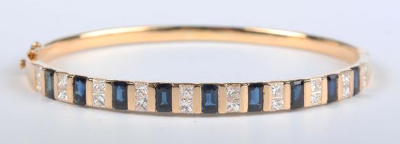 TooveysA gold, sapphire and diamond bangle, mounted with a row of nine cut