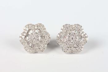 A pair of white gold and diamond earrings, each in a flowerhead shaped design, mounted with circular and tapered baguette cut diamonds, with post and