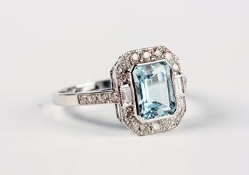 A white gold, aquamarine and diamond cluster ring, collet set with the cut cornered rectangular step cut aquamarine within a surround of baguette and