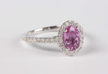 A platinum, pink sapphire and diamond oval cluster ring, claw set with the oval mixed cut pink sapphire within a surround of circular cut diamonds, be
