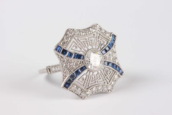 Tooveys|中西方古董藝術(shù)A platinum, sapphire and diamond ring, collet set with the principal circular cut diamond at the centre, otherwise in a pierced millegrain design, det