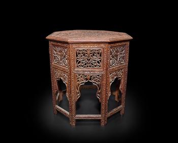 An octagonal carved wood table,?
Madras, India, mid-19th century

The table top fitting onto the hinged folding base, deeply carved to top with a