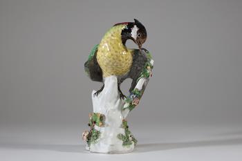 Sujet en porcelaine allemande représentant un oiseau perché sur un tronc fleuri, le plumage finement polychromé et rehaussé d’or, reposant sur une ba